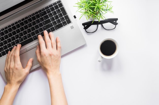 close-up-person-s-hand-typing-laptop-with-coffee-cup-eyeglasses-pot-plant-white-desk_23-2148041861